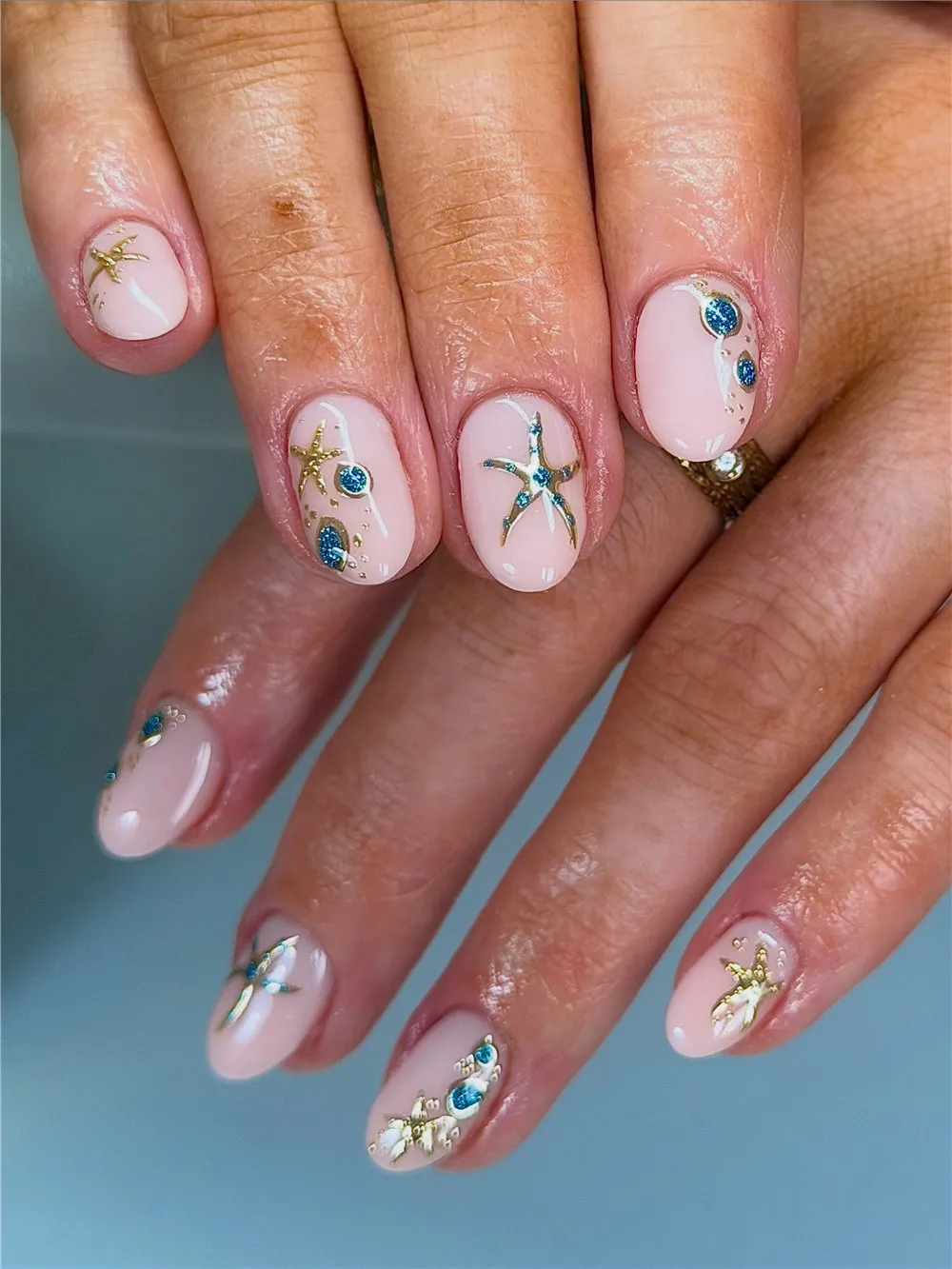 Short 3D ocean nails with gold starfish, blue gems, shells, and nude polish
