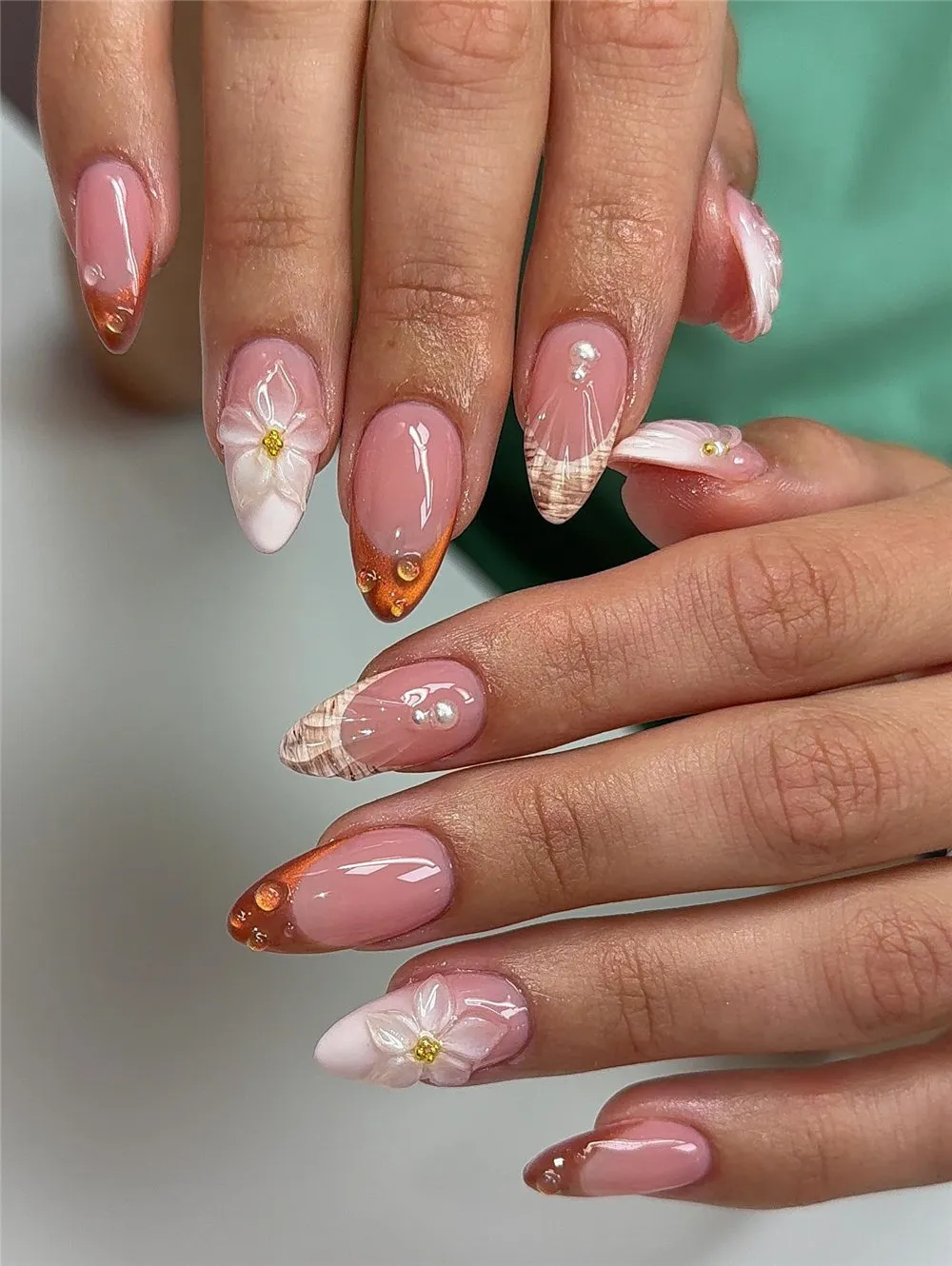 Long almond beach nails with amber tips, shell lines, pearls, and white 3D flowers