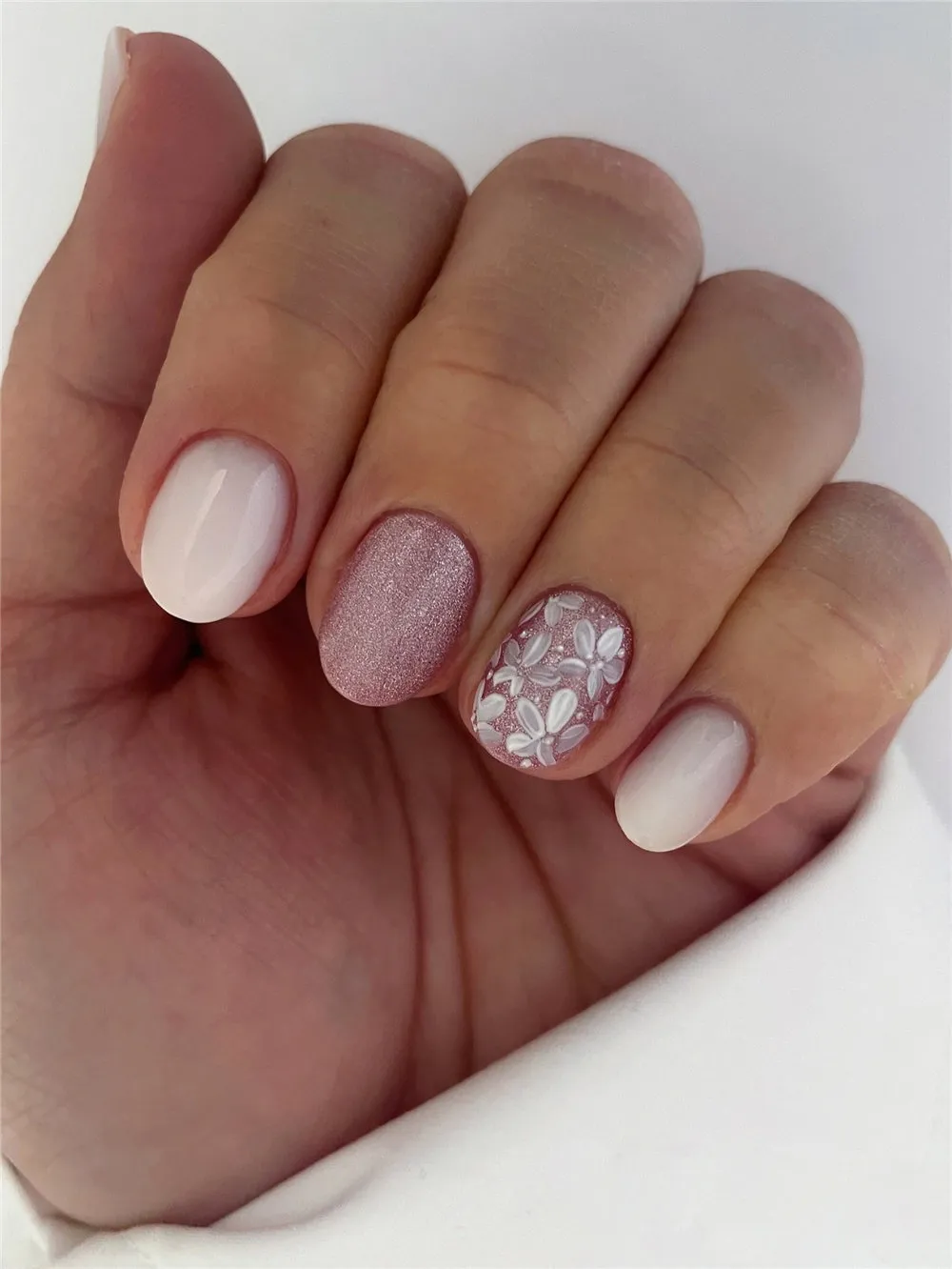 Short white nails with pink glitter and a pink floral accent nail