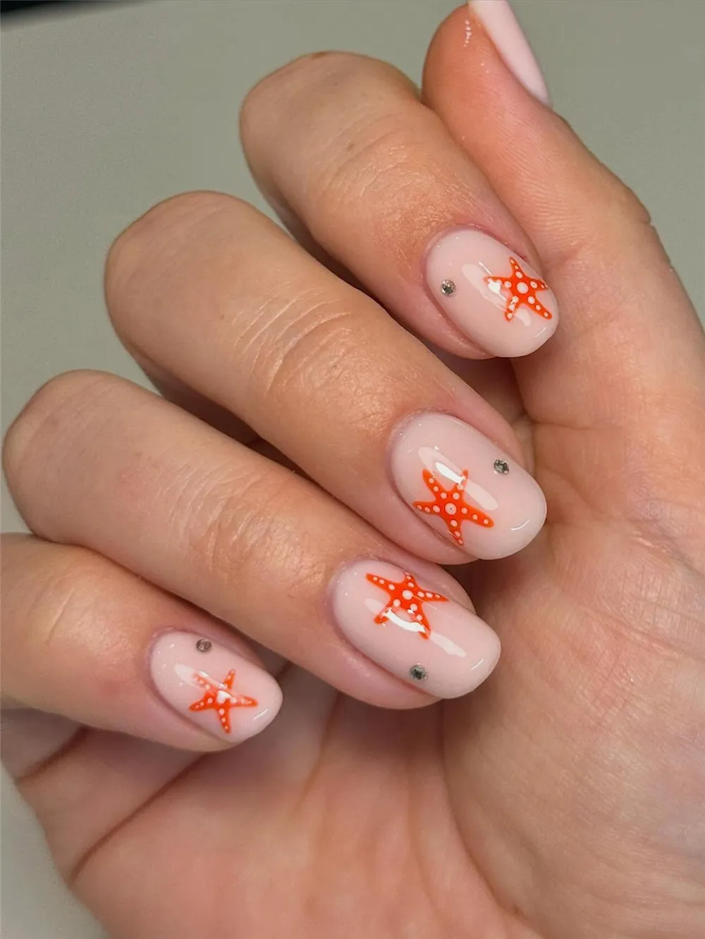 Short milky nude nails with orange starfish and small silver rhinestones