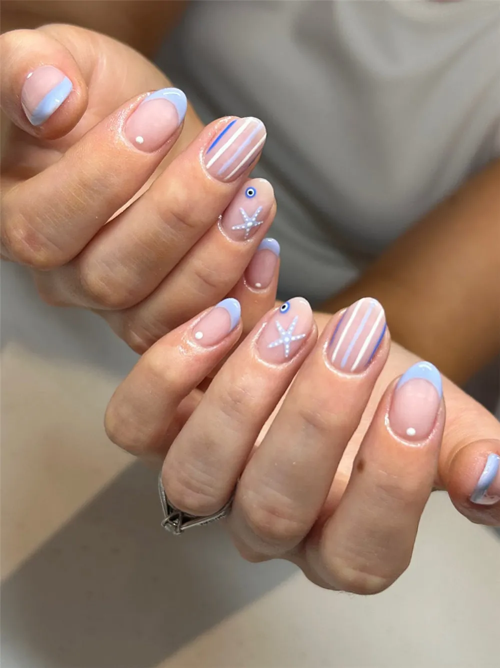 Short light blue holiday nails with starfish, striped accents, and French tips