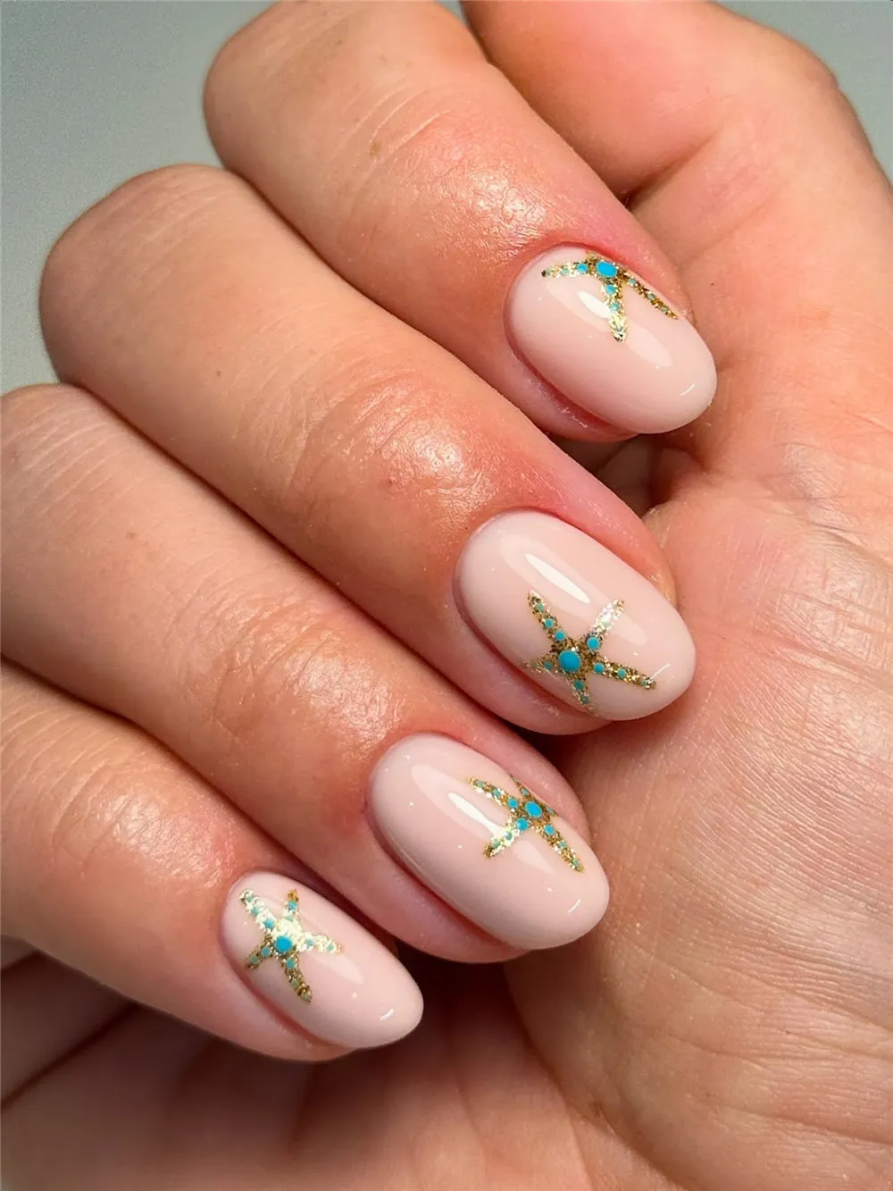 Short oval nude nails with turquoise and gold starfish accents