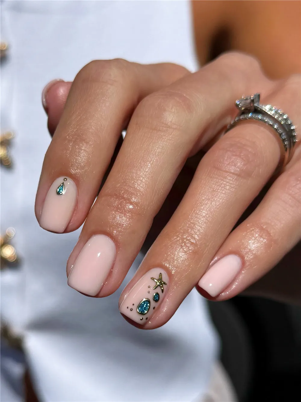 Short pale pink nails with turquoise gems, gold starfish, and tiny dotted accents