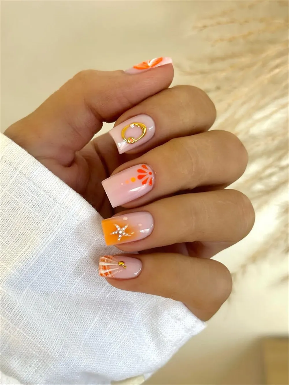 Square orange holiday nails with shell art, gold ring accents, and silver starfish