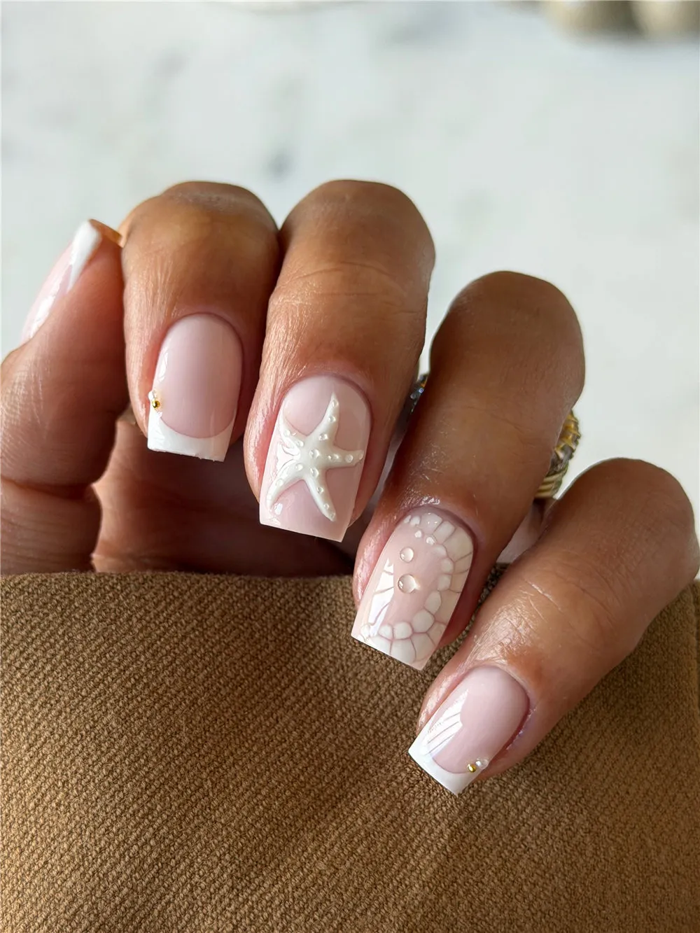 Square nude nails with white French tips, 3D starfish, shell scale art, and gold studs