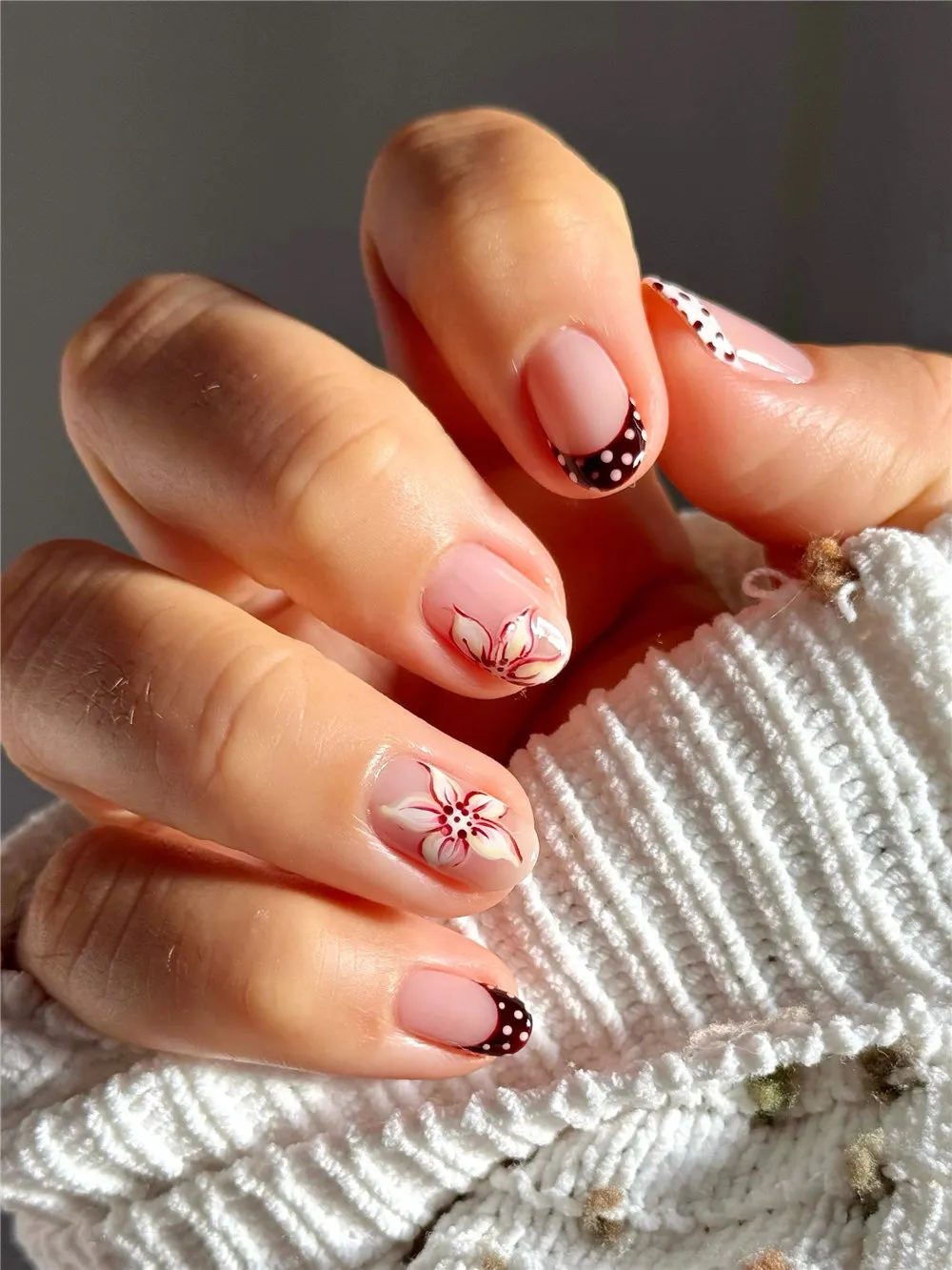 Short nude nails with burgundy polka dot French tips and white flower nail art