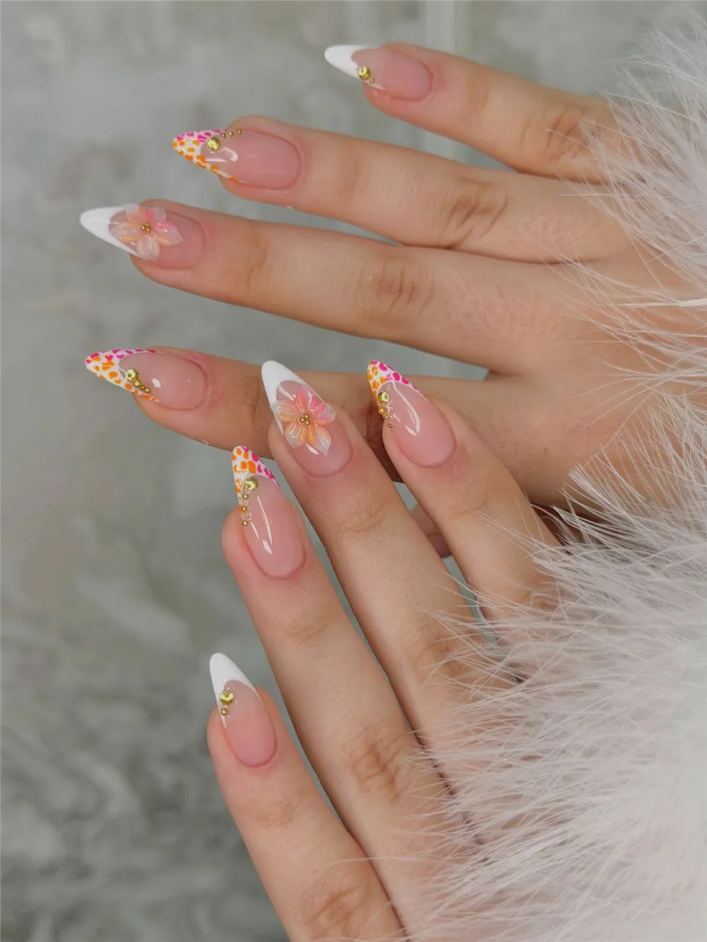 Long almond French tips with orange and pink dots, gold rhinestones, and flower accents