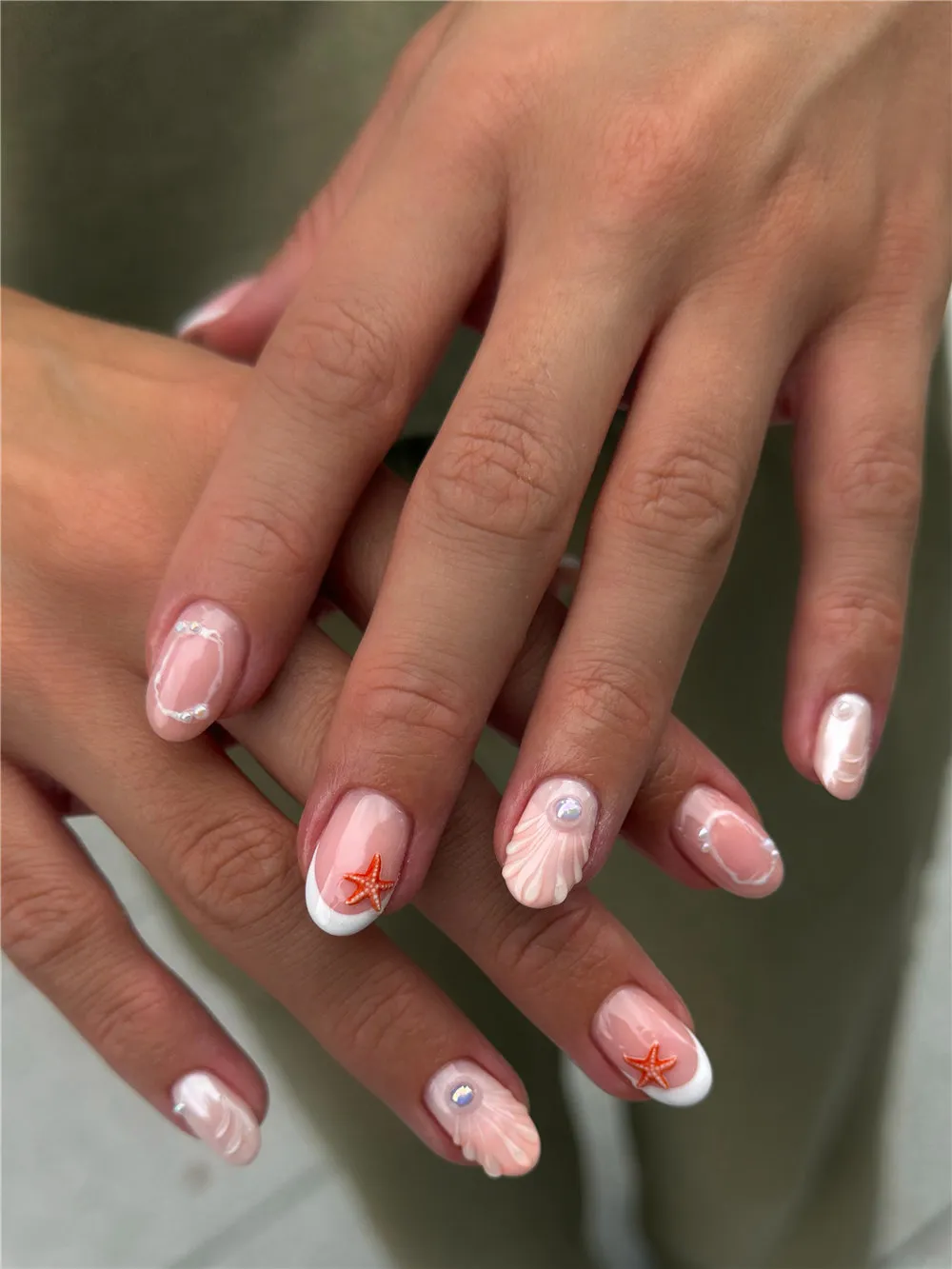 Short French nails with white tips, peach shell texture, pearls, and orange starfish
