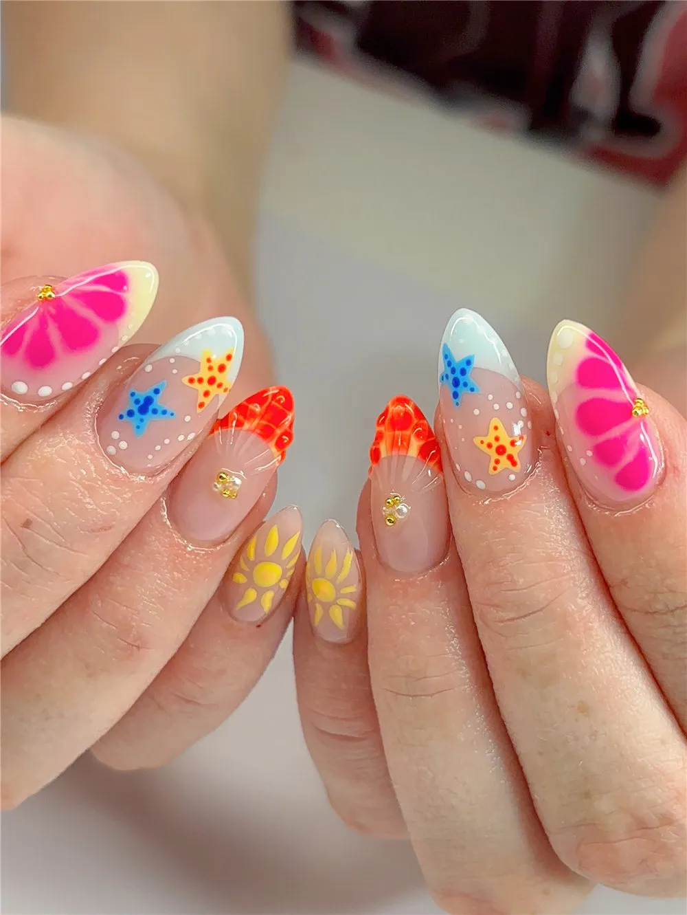 Almond French tips with colorful starfish, sun, shell, and pink flower nail art