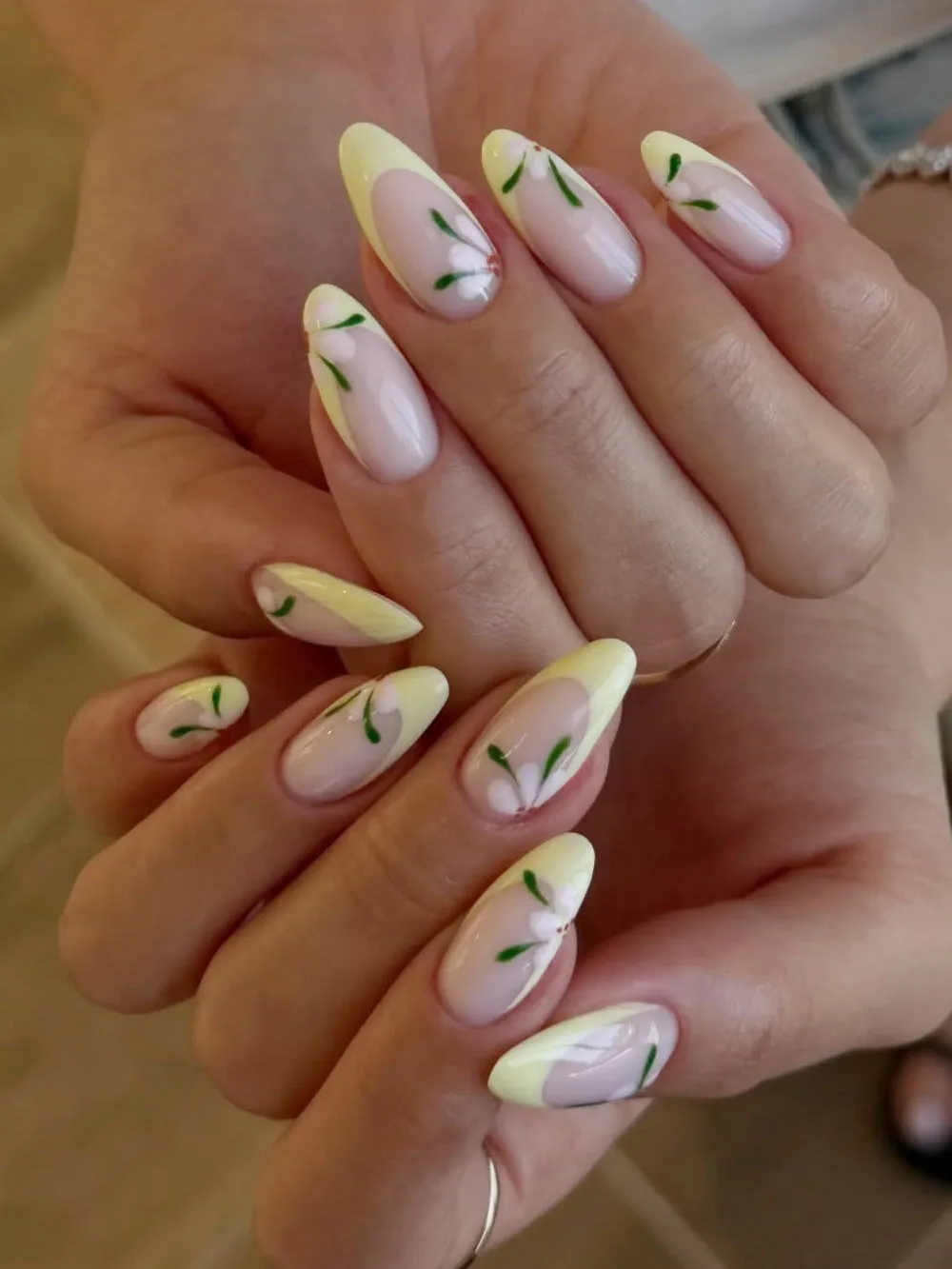 Long almond nails with pale yellow French tips, white flowers, and green leaves