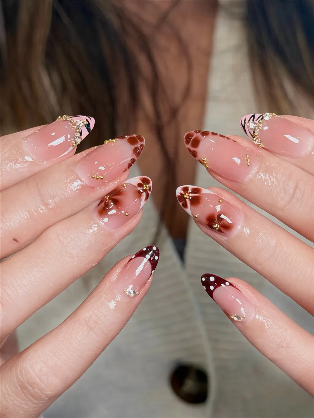 Long almond French tips with brown flowers, burgundy dots, gold beads, and crystals